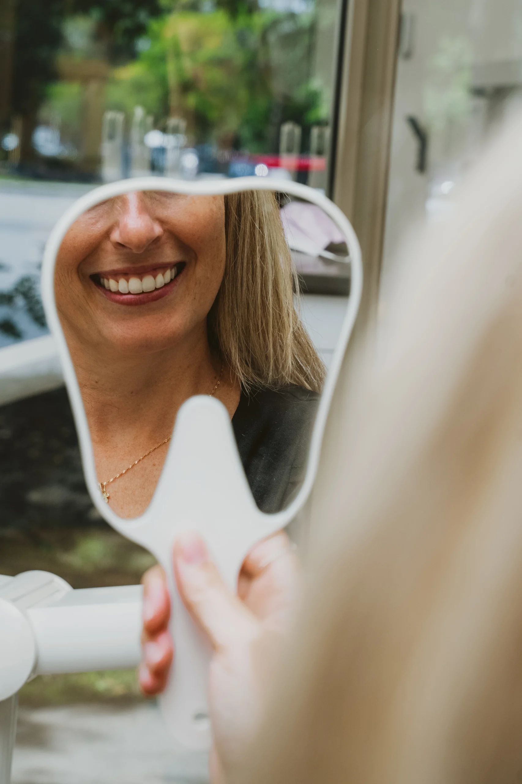 Patiente souriant en observant le résultat de son traitement dans un miroir dentaire