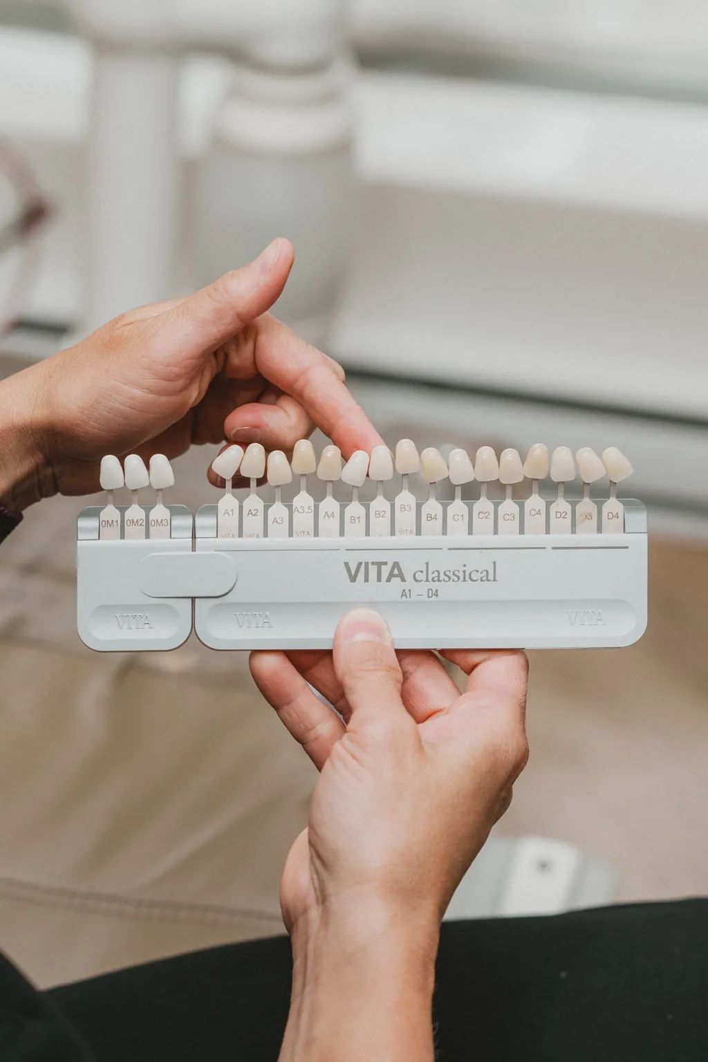 Dentiste utilisant un teintier dentaire pour sélectionner la couleur des dents d’une patiente